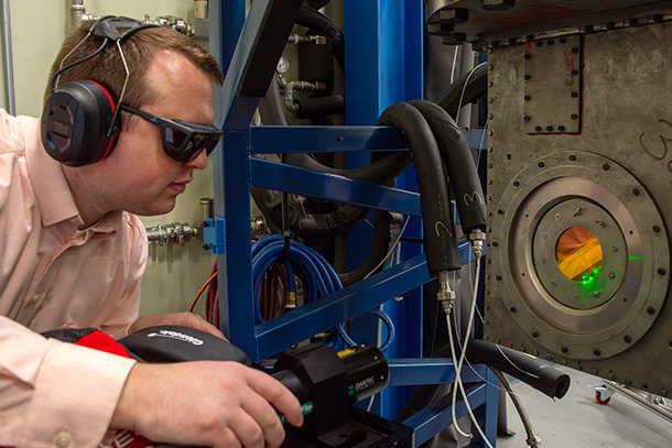 Individual wearing safety goggles and ear protection uses lab equipment. 